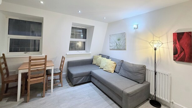 A modern living room with a grey sofa, wooden chairs, a dining table, and a floor lamp. - Flat in Bethnal Green (London)