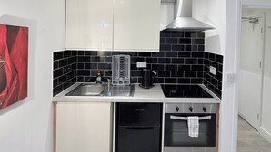 A compact kitchen with a black tiled backsplash, white cabinets, a stainless steel sink, a coffee machine, and a built-in oven. - Flat in Bethnal Green (London)
