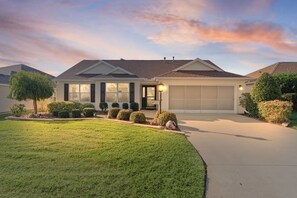 A single-story house with a garage, a well-maintained lawn, and a variety of shrubs and trees. - 3/2 Designer in the Village of Poinciana (The Villages)