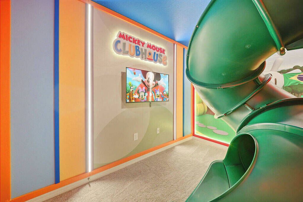 A colorful interior with a Mickey Mouse Clubhouse sign, a play area with green slides, and a carpeted floor.