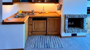 Een compacte keuken met houten kastjes, een ingebouwde magnetron, een gasfornuis en een stenen openhaard.