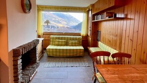 Een gezellige kamer met een open haard, een houten eettafel en uitzicht op bergen door een raam.