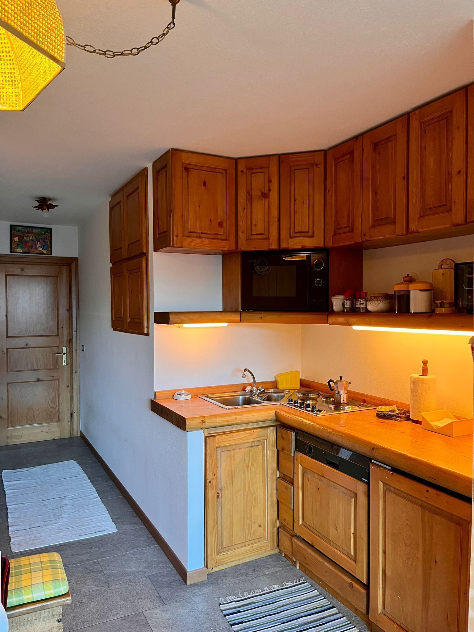 Una cocina compacta con gabinetes de madera, un microondas y un lavamanos.