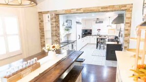 Een moderne keuken met een accentmuur van steen, een eethoek met een houten bank en een zichtbaar keukeneiland.