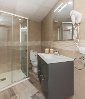 Un baño moderno con cabina de ducha de vidrio, un lavabo blanco y un secador de pelo montado en la pared.