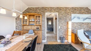 Un coin repas avec une table en bois, des chaises et un buffet aux portes vitrées. Un tapis noir recouvre le sol, et un tableau est visible au mur.