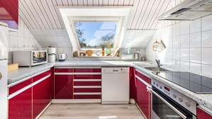Une cuisine moderne avec des meubles de rangement rouges, un lave-vaisselle, un four à micro-ondes, une machine à café et une grande fenêtre.