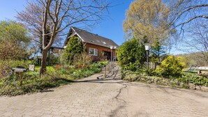 Un chemin menant à une maison aux murs en briques, entourée de verdure et sous un ciel dégagé.
