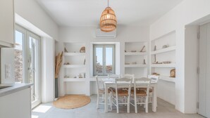 A modern kitchen with white cabinetry, a dining table with chairs, and a hanging light fixture. - Villa 'Farous Seaside Sunset' with Sea View, Wi-Fi and Air Conditioning (Antiparos)