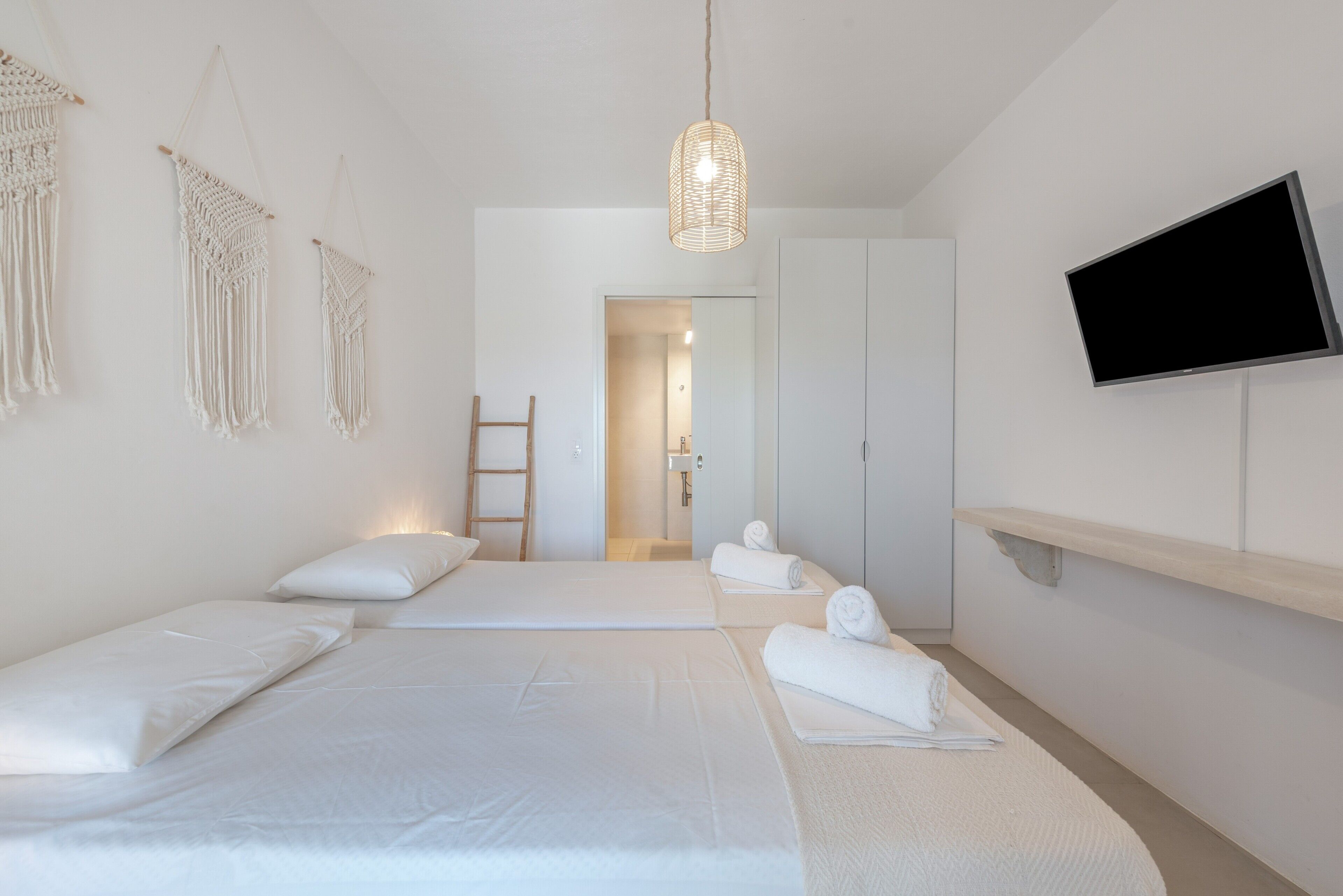 Een minimalistisch hotelkamer met twee bedden, een televisie, macramé wanddecoratie en een ladder.