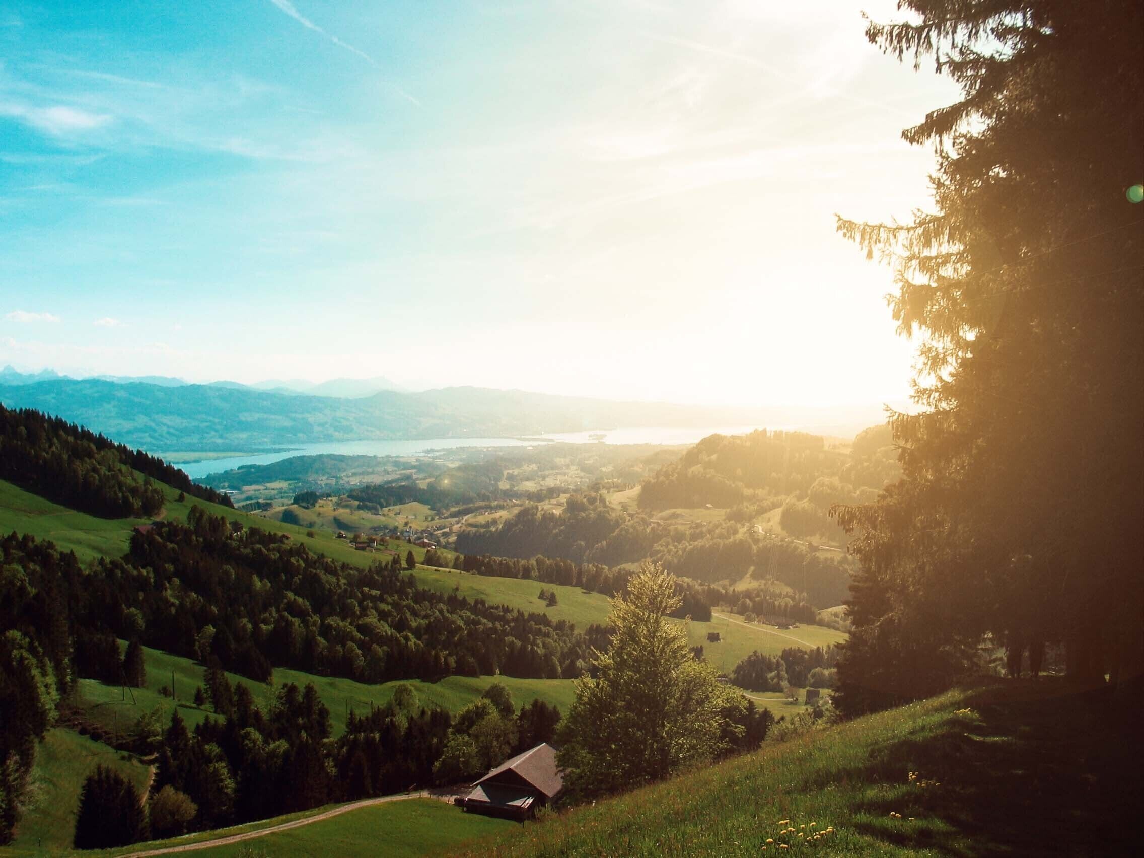 A rural landscape with rolling hills, a small cabin, and a lake in the distance.