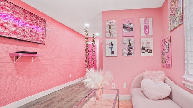 A pink-themed room with a flat-screen TV, a glass coffee table, and a pink sofa with a heart-shaped pillow. - Pink Mini Unit With Pool in Philly (Philadelphia)