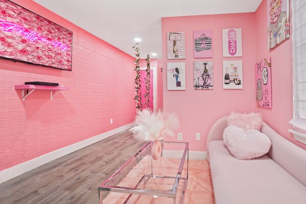A pink-themed room with a flat-screen TV, a glass coffee table, and a pink sofa with a heart-shaped pillow. - Pink Mini Unit With Pool in Philly (Philadelphia)
