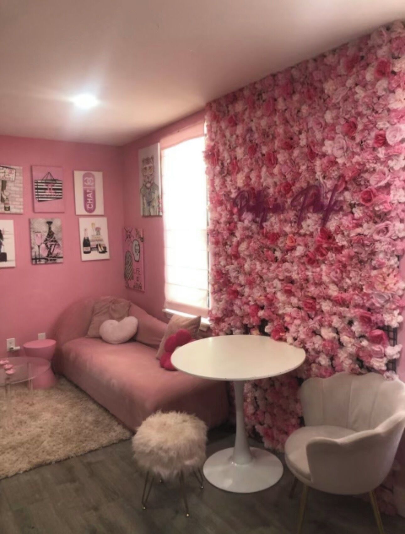 A pink-themed room with a sofa, a round table, a fluffy stool, and a chair.