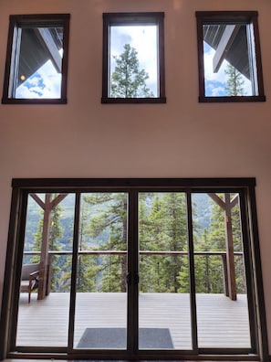 A room with three windows and a large sliding door leading to an outdoor deck with a view of a forested mountain. - San Juan Backcountry Lodge, Brand New Luxury lodge near Silverton Colorado (Silverton)