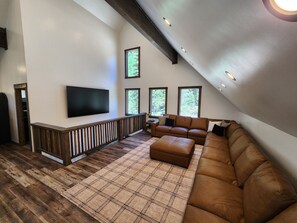 Un'ampia zona giorno con un divano componibile, una TV a schermo piatto montata a parete e una ringhiera in legno.