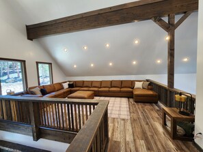 Een ruime loft met een grote L-vormige zithoekbank, houten balken en een houten terras.