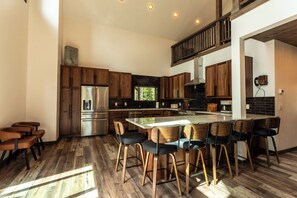 Una cocina moderna con una isla central, armarios de madera, electrodomésticos de acero inoxidable y un comedor con taburetes de bar.