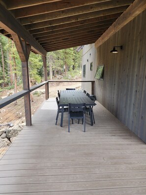 Eine überdachte Terrasse mit Holztisch und -stühlen, umgeben von einem Holzaum, mit Blick auf ein bewaldetes Gebiet.