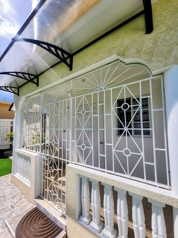 A house with a covered porch, a white metal gate, and a stone-tiled entrance. - Norwick Bliss (Montego Bay)