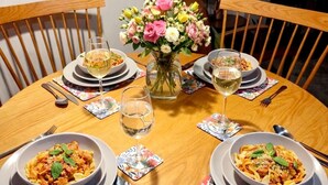 Ett matbord dukat med tallrikar fyllda med pasta, glas med vitt vin och en vas med blommor.