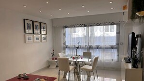 Un salón moderno con comedor, que incluye una mesa de vidrio, sillas blancas, una mesa de centro roja y cuadros en la pared.
