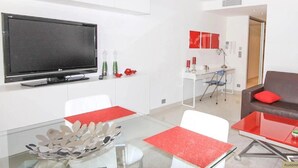 Una sala moderna con un sofá marrón, cojines rojos, una mesa de centro de vidrio y un televisor de pantalla plana montado en la pared.