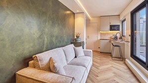 Una sala moderna con un sofá, una zona de cocina con microondas y un ventanal grande.