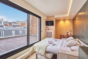 Una habitación de hotel moderna con un balcón amplio, una cama con sábanas blancas, un televisor y una mesita de noche de madera.
