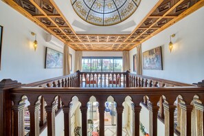 Eine imposante Treppe mit aufwendigen Holzschnitzereien, eine hohe Decke mit geometrischen Mustern und ein Blick ins Freie.