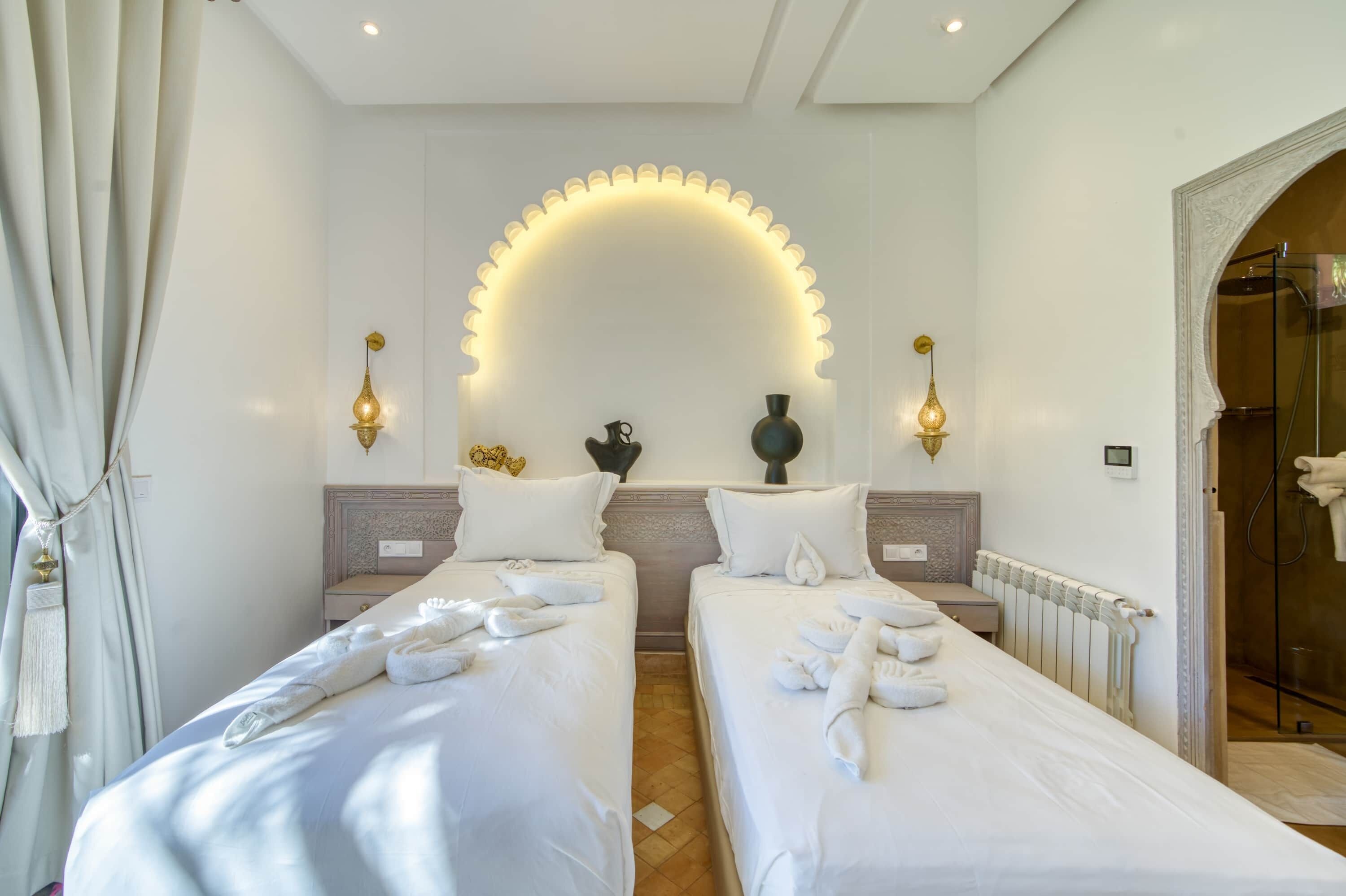 A hotel room with two beds, a shower, and a large arched light fixture.