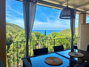A balcony with a glass table, wicker chairs, and a view of a mountainous landscape and ocean. - Four-room apartment 3 bedrooms, 2 bathrooms and sea view terrace (Rio Nell'elba)