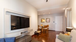 A modern living room with a flat-screen TV mounted on the wall, a sofa, a dining area with a table and chairs, and a lamp. - Near Rodrigo de Freitas Lagoon Pc308 (Rio de Janeiro)