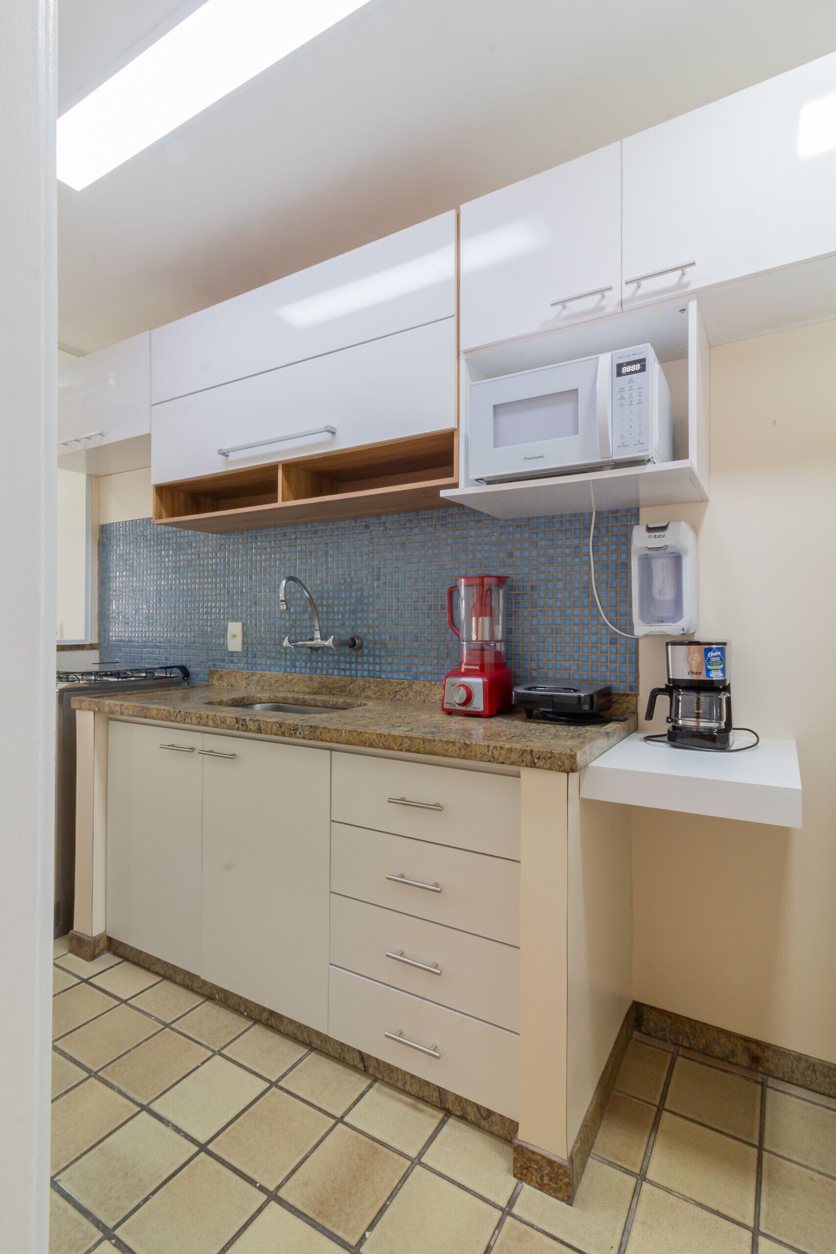 A kitchen with white cabinets, a blue tiled backsplash, a granite countertop, a red blender, a coffee maker, and a microwave.