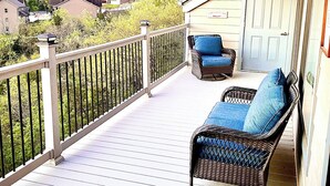 Eine überdachte Veranda mit weißer Reling, ein Korbsessel mit blauen Kissen und im Hintergrund eine Ansicht von Häusern und Bäumen.