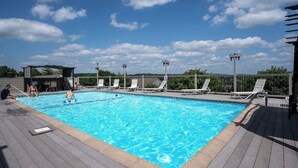 Ein rechteckiger Pool mit klarem, blauem Wasser, umgeben von einer Holzterrasse. Liegestühle und eine überdachte Sitzgelegenheit sind vorhanden.