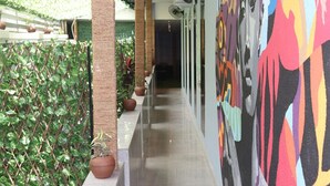 A corridor with a green hedge on one side, a row of potted plants, and a colorful abstract mural on the wall. - CORA HOMES (Jos)