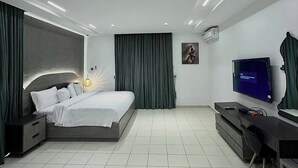 A modern bedroom with a large bed, a desk, a television, and a wall-mounted air conditioner. - CORA HOMES (Jos)