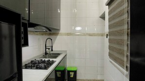 A compact kitchen with white tiles, a gas stove, a sink, and two trash bins. - CORA HOMES (Jos)