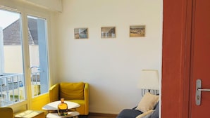 A modern living room with a yellow armchair, a blue sofa, and a small round table with a vase. There are three framed pictures on the wall and a red door. - In the heart of Hardelot, 2 minutes' walk from the beach. Renovated 5-person apartment (Neufchâtel-Hardelot)