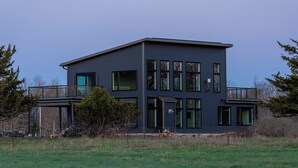 Una casa moderna de dos pisos con balcón, ventanas grandes y techo plano.