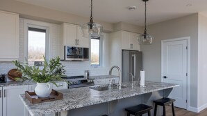 Cocina con gabinetes blancos, encimera de granito, refrigerador de acero inoxidable e iluminación colgante.
