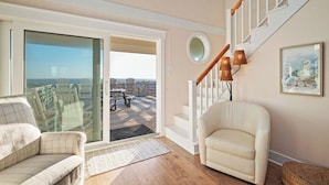 A living room with a sofa, armchair, and a staircase leading to a balcony. - Pickled Pelican: Bright and Airy Oceanfront Home (Oak Island)