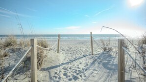 A sandy beach path with wooden posts and rope barriers leading to the ocean. - Pickled Pelican: Bright and Airy Oceanfront Home (Oak Island)