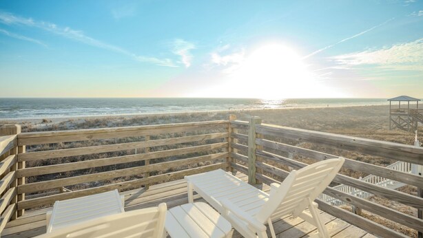 A wooden deck with white chairs overlooking a beach and ocean. - Pickled Pelican: Bright and Airy Oceanfront Home (Oak Island)