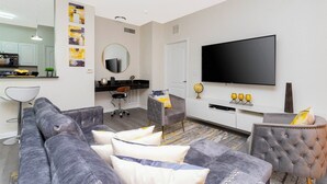 Ein modernes Wohnzimmer mit einem grauen Sofa, einem Fernseher und einer im Hintergrund sichtbaren Küchenzeile.