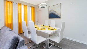 Ein Essbereich mit einem weißen Tisch, gedeckten Plätzen für vier Personen, gelben Platzsets und weißen Stühlen.