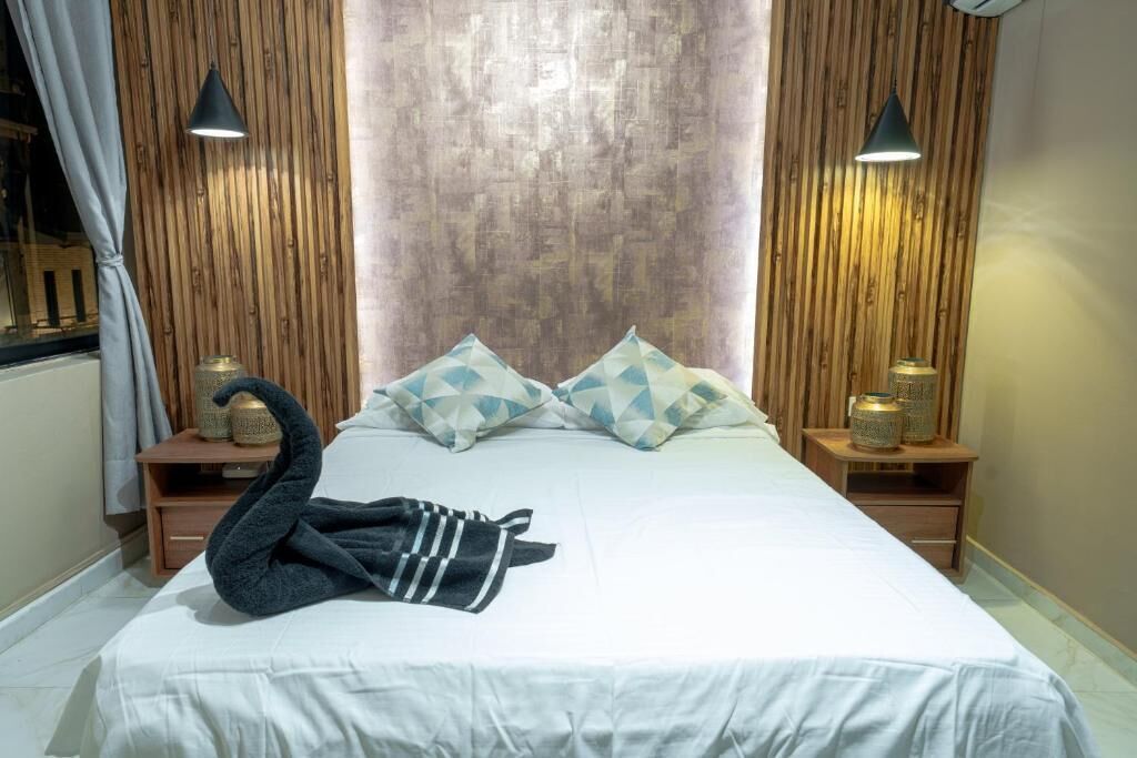 A neatly made bed with geometric pillows, a swan-shaped towel, and bedside lamps on wooden nightstands.