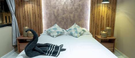 A neatly made bed with geometric pillows, a swan-shaped towel, and bedside lamps on wooden nightstands.