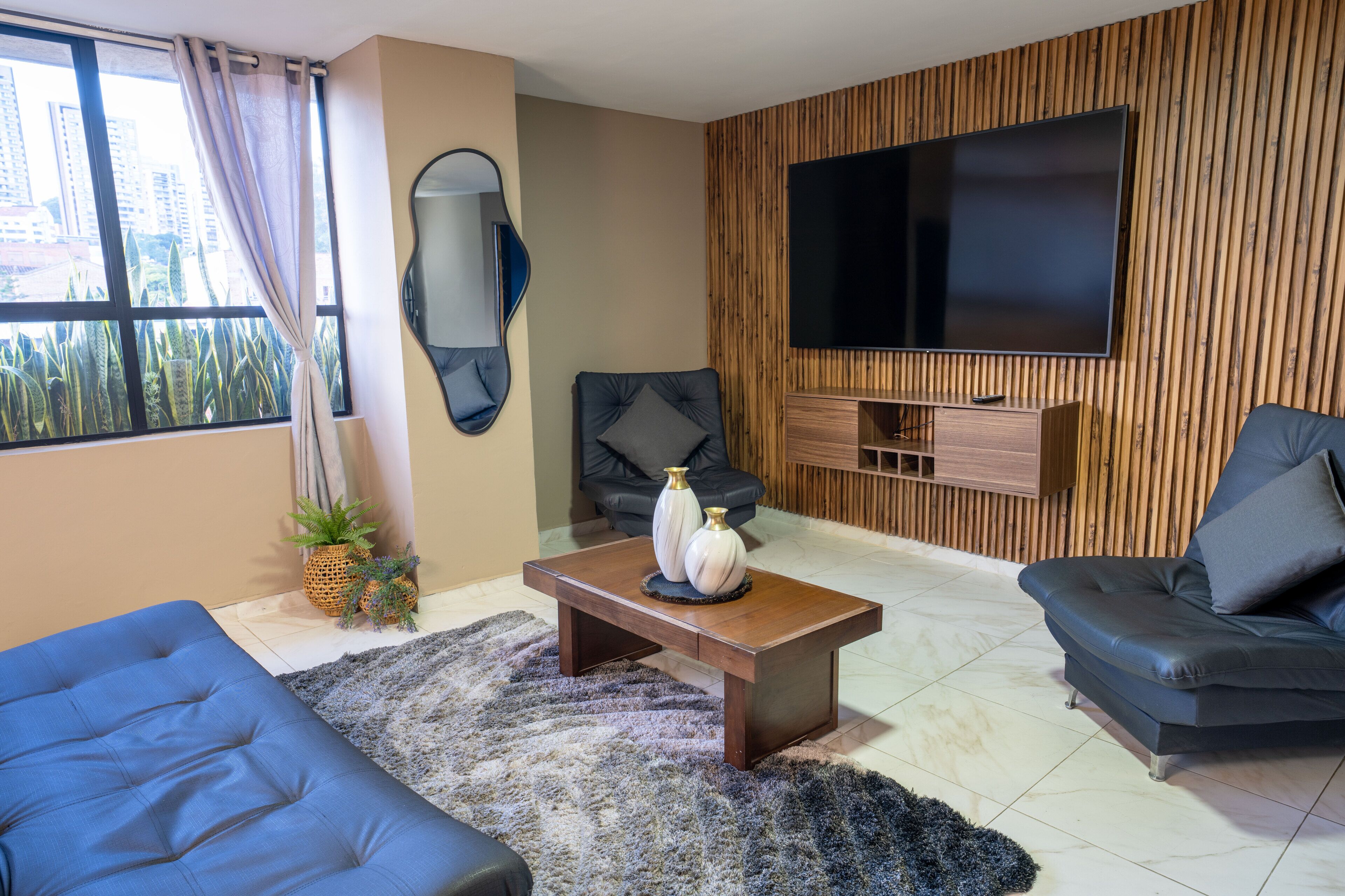 Un salon moderne avec une grande télévision, un canapé, une table basse et une vue sur les bâtiments environnants.